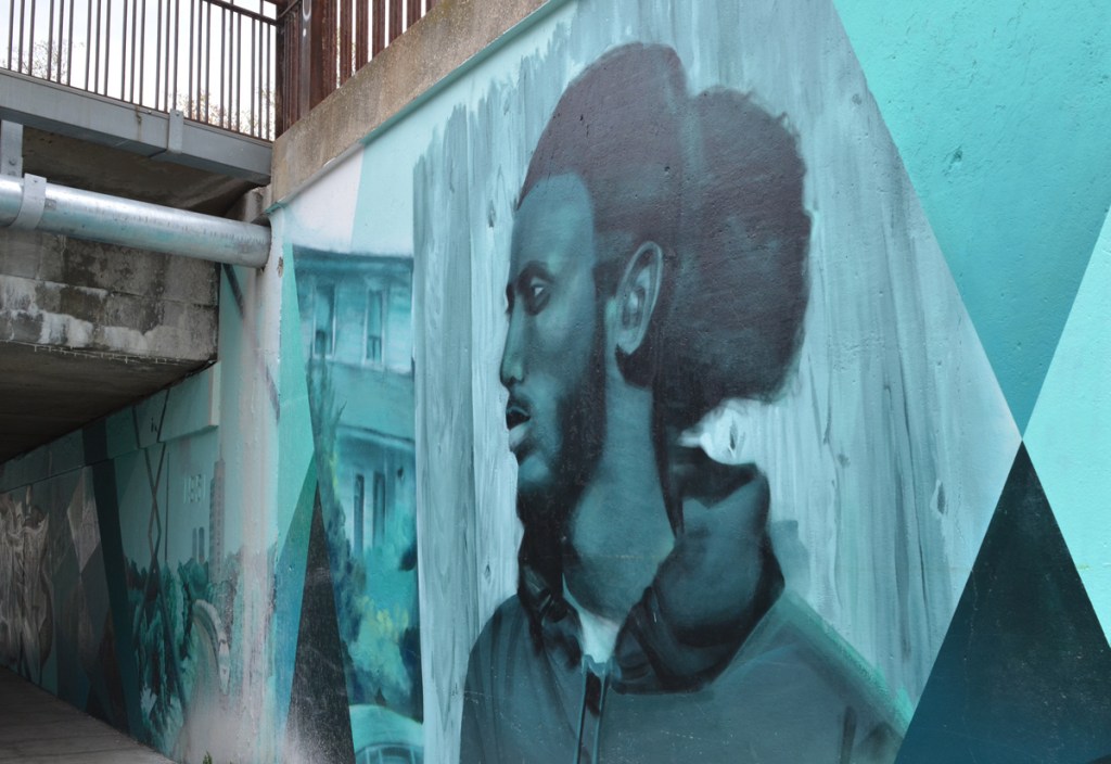 painting of a young black man in a mural on Jones Ave., with railway overpass