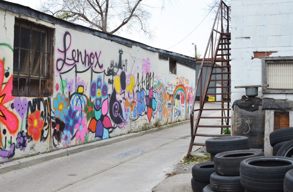alleyway with metal exterior stairs to upper floor, a pile of tires, and a wall full of colourful flowers and a rainbow 