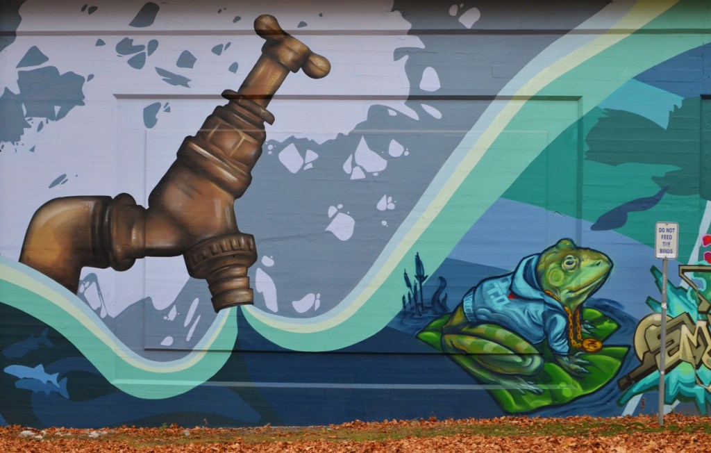 part of a mural, a very large brass faucet is open, water is pouring out, a frog sits on a lily pad