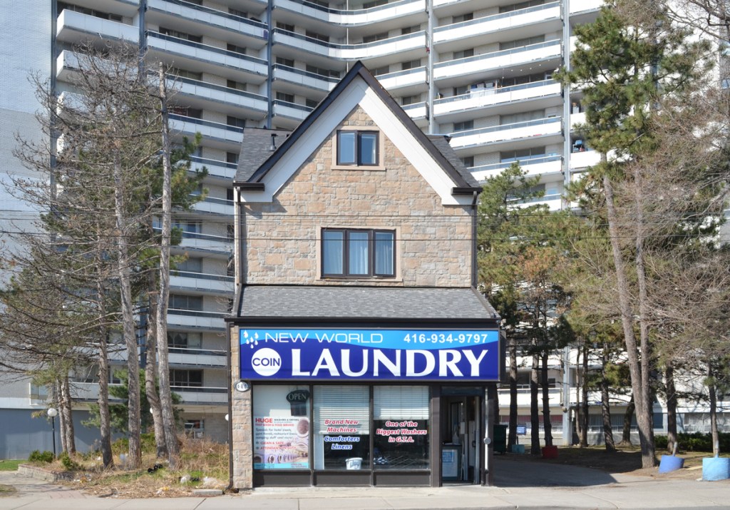 an older single family house now the New World laundry, stands alone with a St. James Town highrise behind it 