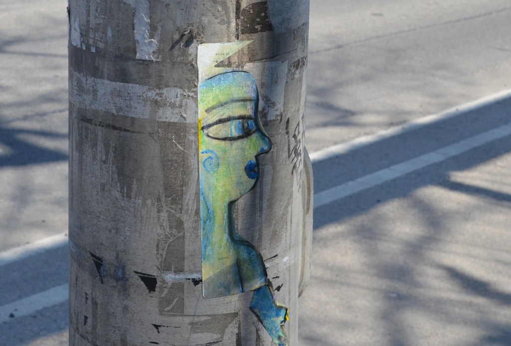 paste up graffiti on a pole, a drawing of a portrait of a woman in profile, drawn in black but shaded in blues and greens