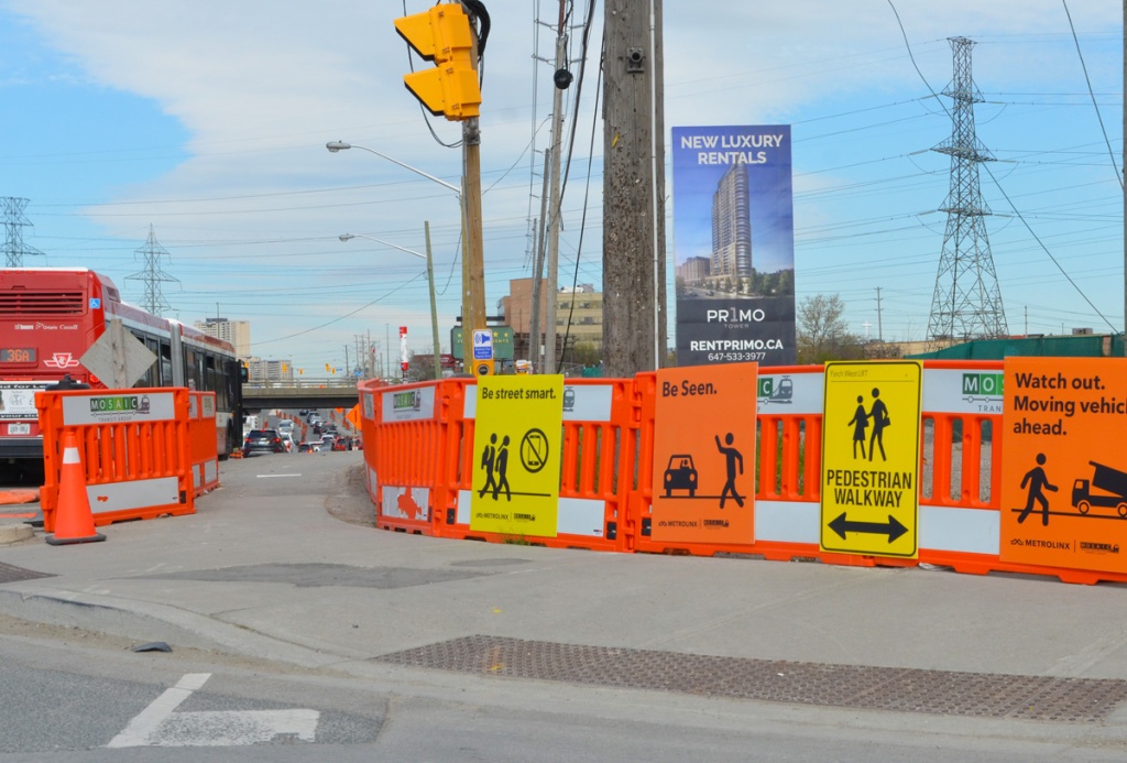 large yellow and orange signs guide pedestrian track through a busy intersection with a lot of construction