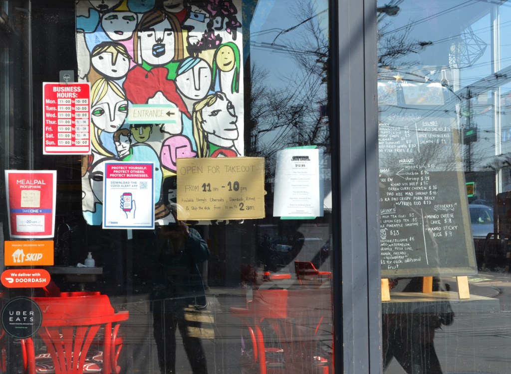 signs and pictures in the window of a restaurant, open for takeout from 11 a.m. to 10 p.m. 