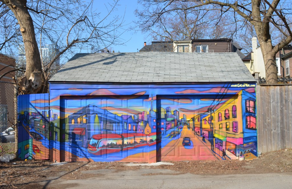 a mural of a toronto street with a TTC streetcar on it, over two garage doors in a small Cabbagetown lane