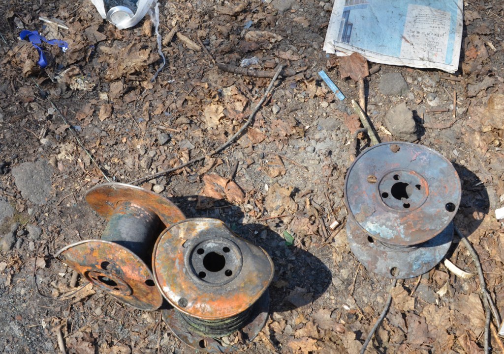 garbage left on the ground, an old newspaper, empty pop can, empty spools for cables or wires