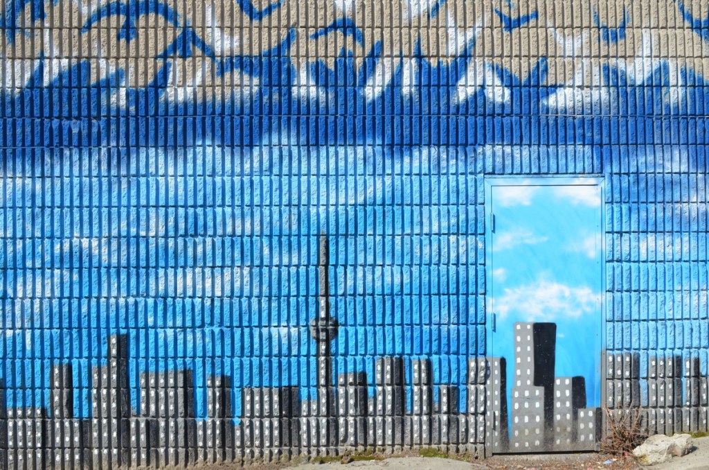 mural of blue birds flying above blue sky and CN tower and toronto skyline, exterior wall with a door in it