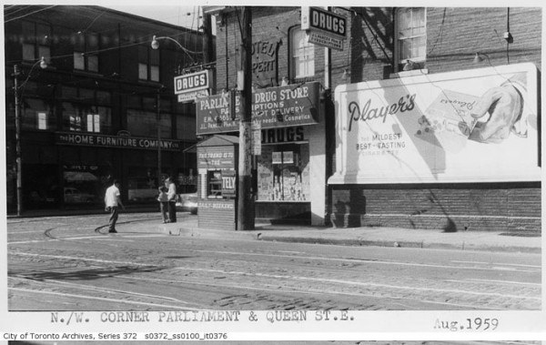 black and white photo from City Archives showing northwest corner of Parliament and Queen with the Rupert Hotel, also the Parliament Drug Store on the ground floor.  A billboard with an ad for Players cigarettes is on the wall of the building