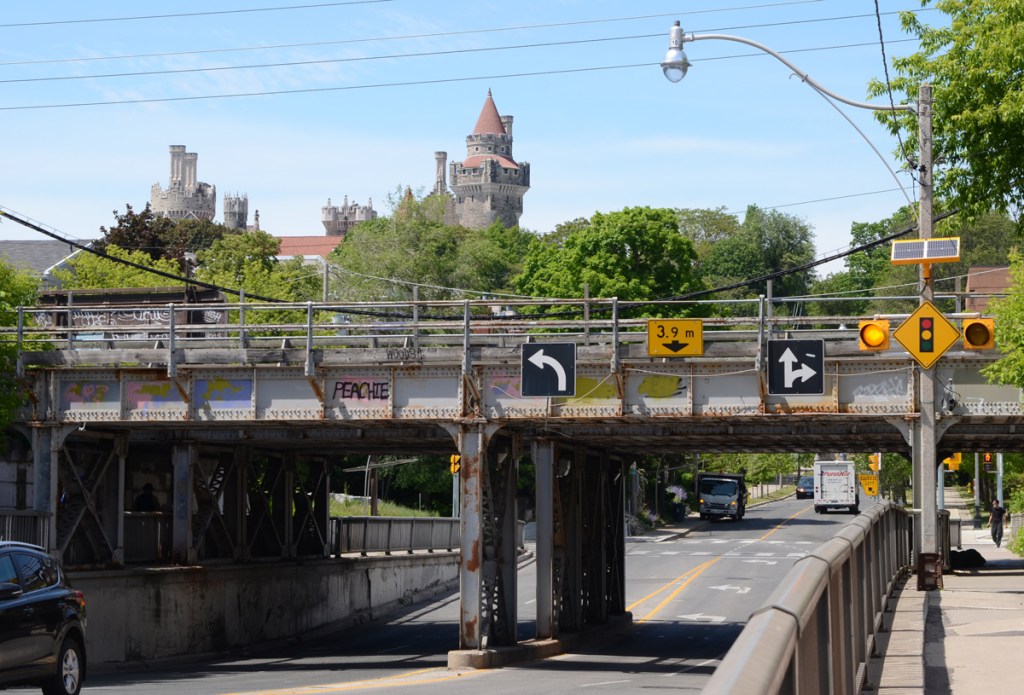 the towers and turret of Casa Loma in the background behind a railway overpass just north of Dupont.