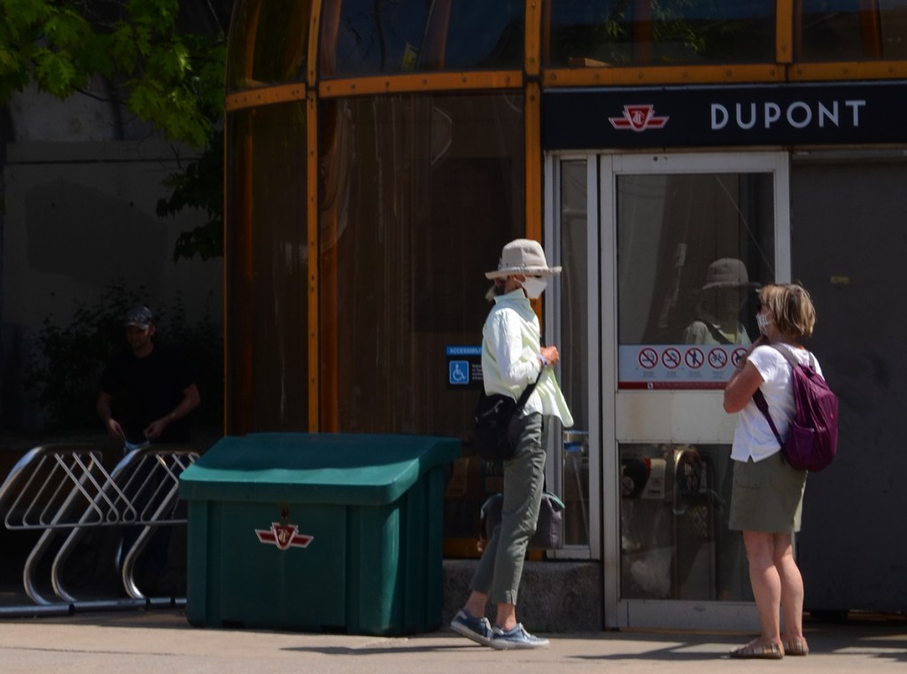 Two women stand talking outside the entrance to Dupont TTC subway station