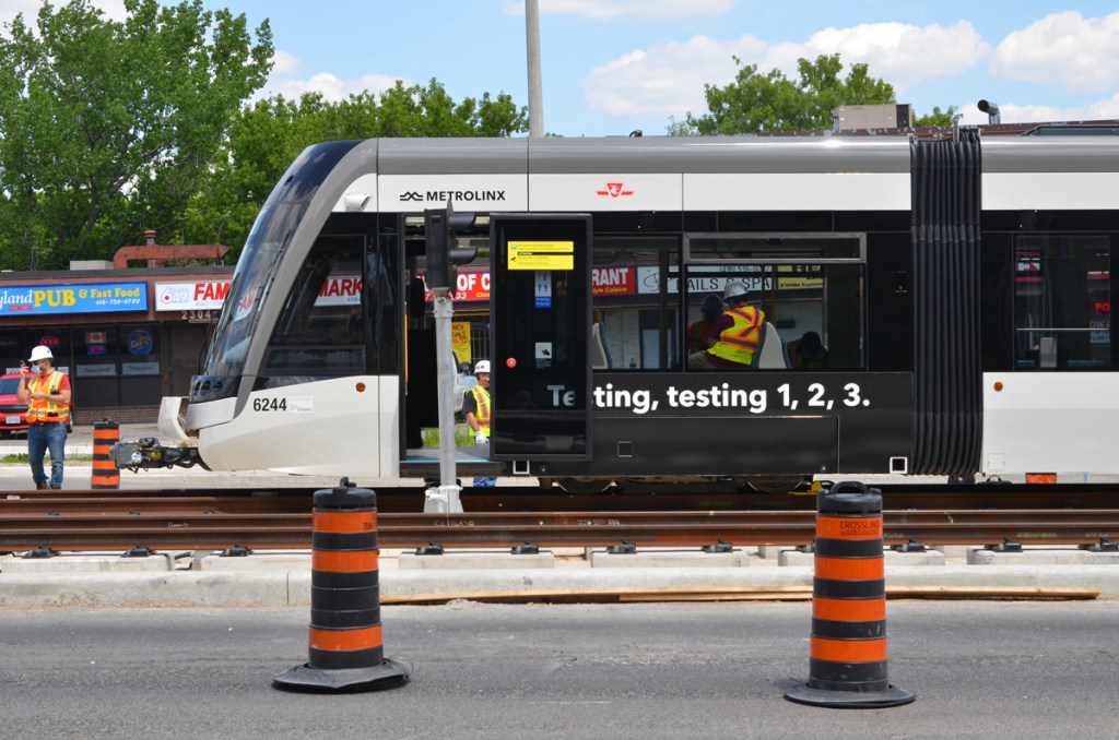 One end of a new TTC LRT train with workmen in yellow and orange safety vests