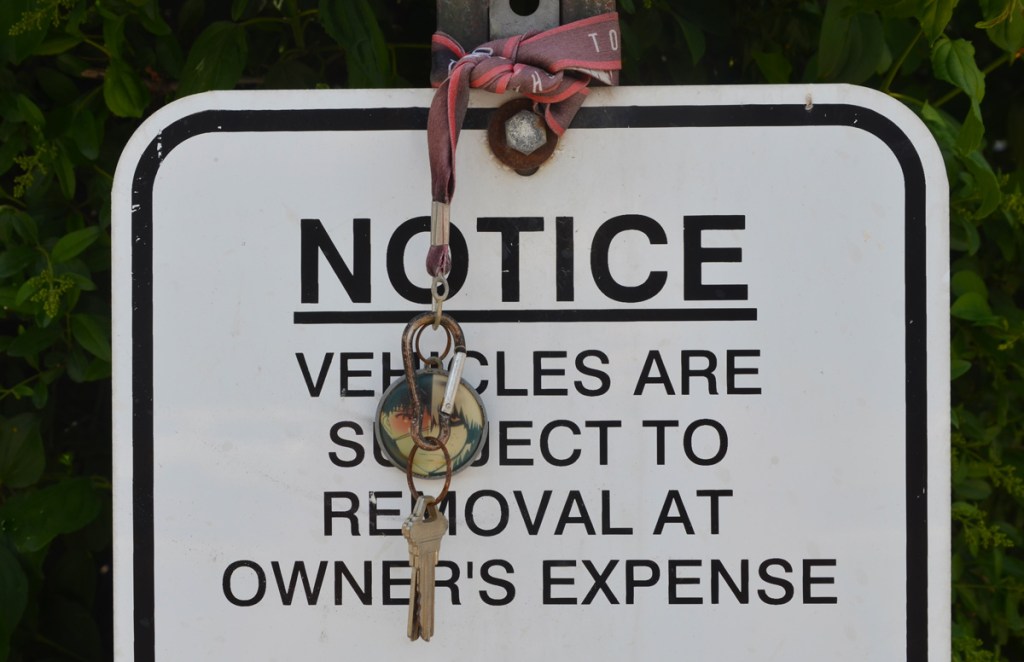 two keys on a ribbon have been tied to a street sign that says notice vehicles are subject to removal at owners expense