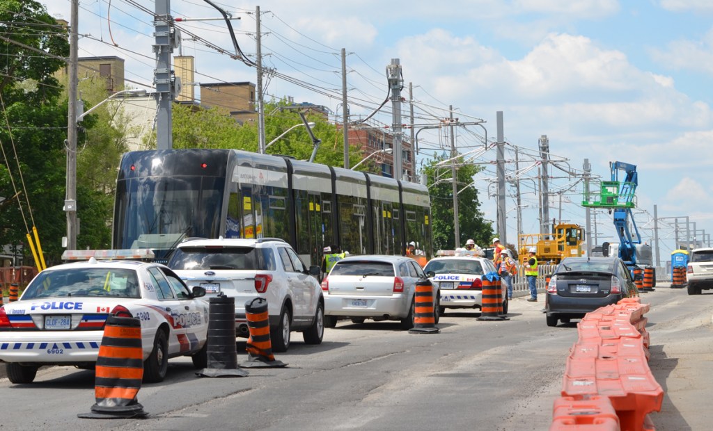 police cars and other cars parked in left lane of traffic, along side new LRT train