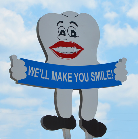 picture of a large tooth with a big red lips and shiny white teeth holding a blue banner that says we'll make you smile 