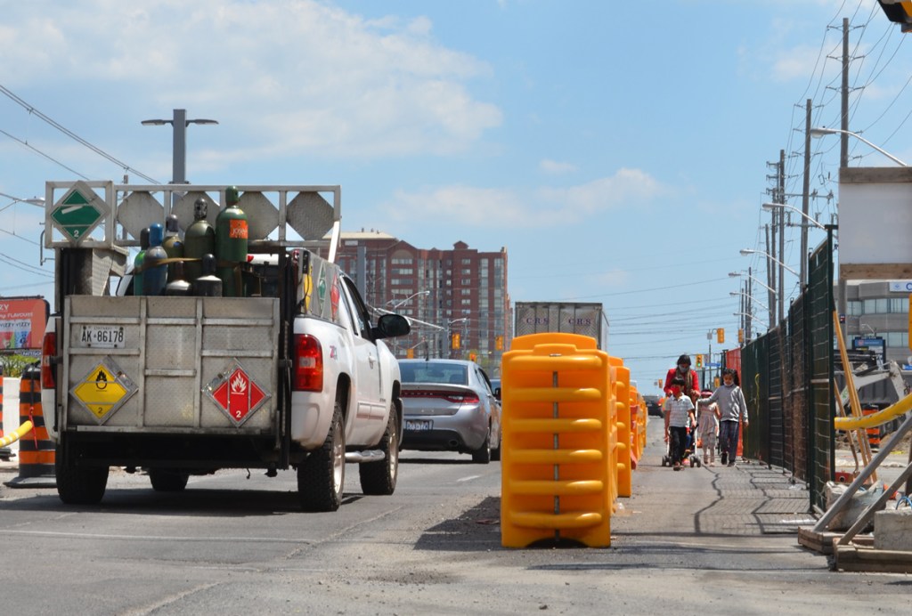 people walking on edge of road that has been separated from traffic by yellow plastic dividers, through construction zone, a mother and her children