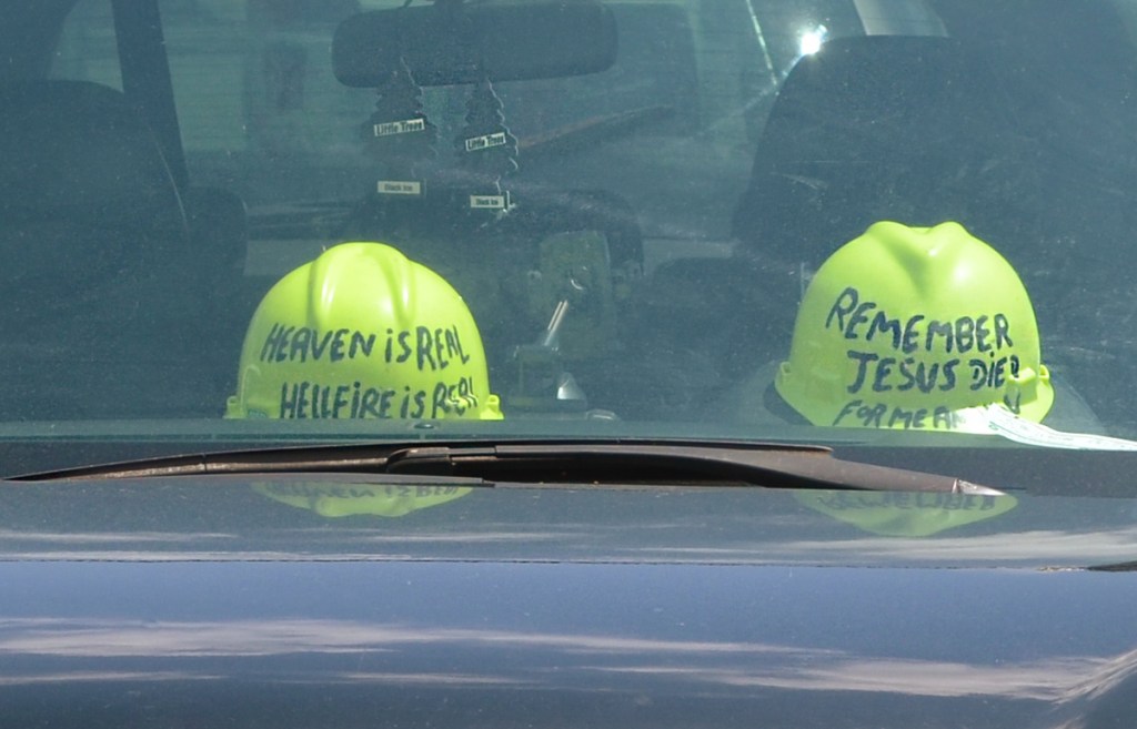 2 hard hats inside a car.  Both yellow. One says Heaven is real Hellfire is Real. and the other says Remember Jesus died for me and you