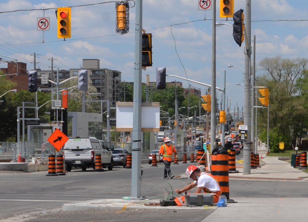 a workman sits on the sidewalk as he works with underground cables at construction site for new LRT on Eglinton