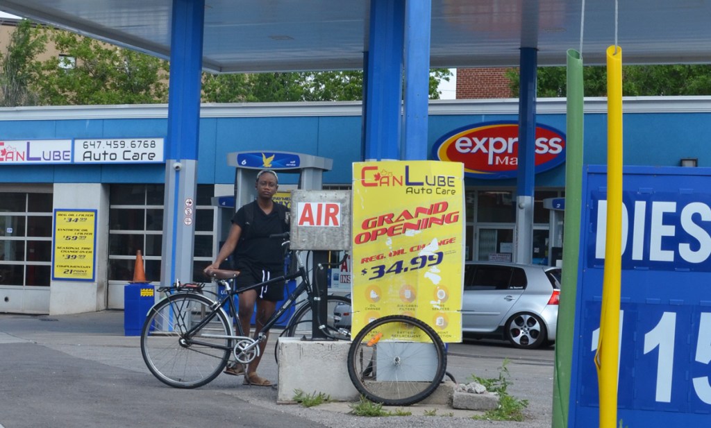 a woman dresses in black t shirt and shorts and holding her bike is getting sir from an air pump at an ultramar service center 