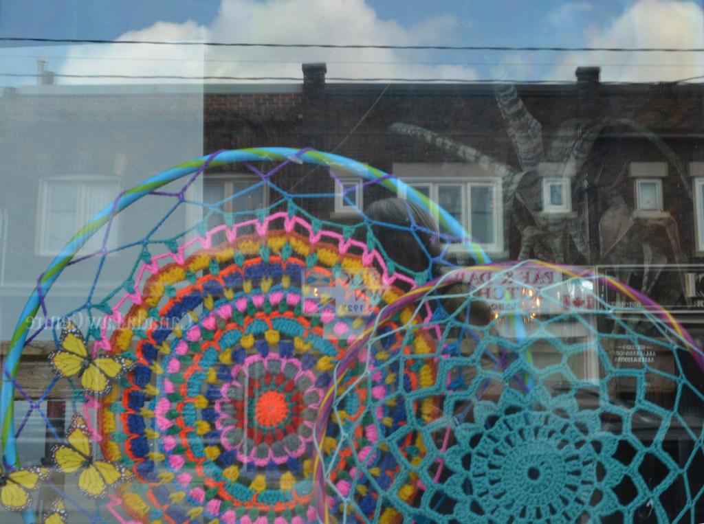 crocheted concentric circles in a window with reflections of the houses across the street