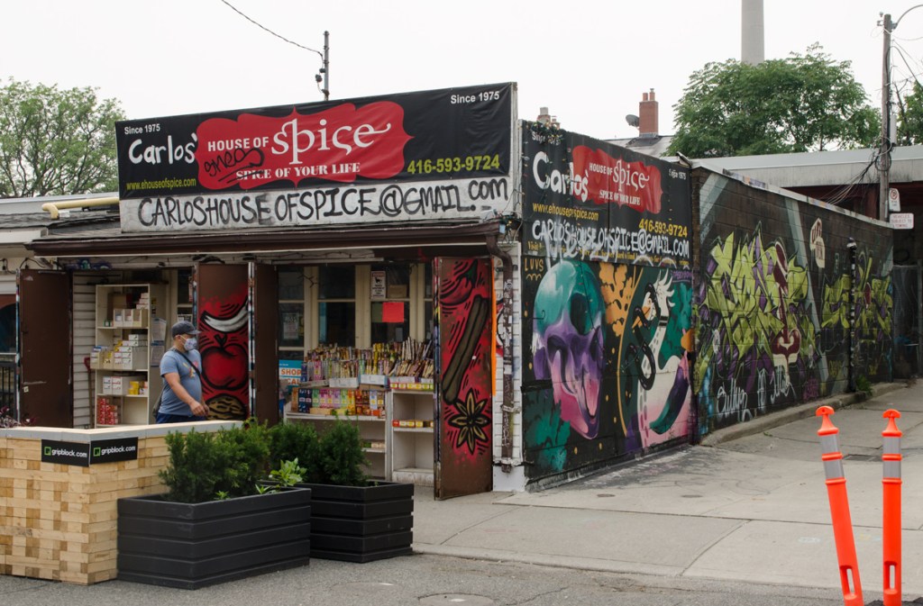 Carlos House of Spice in Kensington, with an alley beside it, murals on the walls in the alley, incense for sale in front,