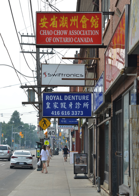 stores and signs on Dundas West near Augusta. Chao Chow Association of Ontario, Swiftronics, Royal Denture, and others, some people walking on the sidewalk too