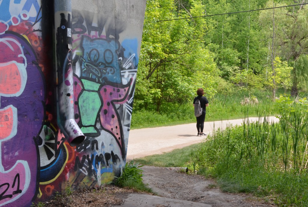 woman walking on path in ravine park, with graffiti on wall behind her 