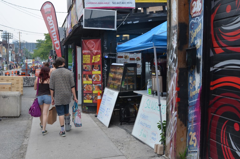 a couple carry their shopping in bags as they walk on sidewalk, walking past