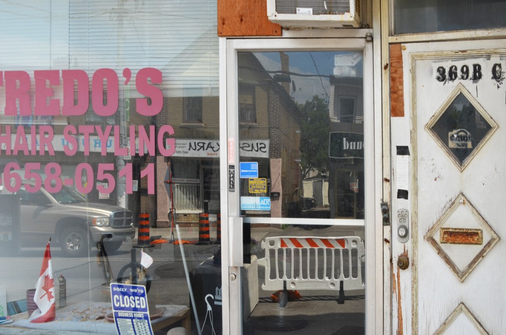reflections in the window of Alfredos hair styling, closed, with a small Canadian flag in the window 