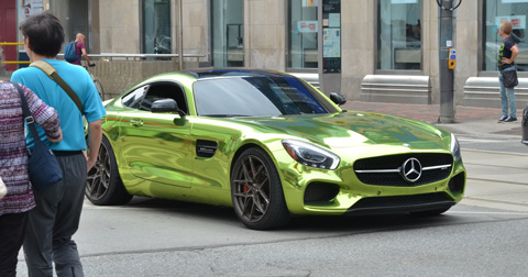 a very shiny metallic green mercedes sports car with no front licence passes through an intersection as a couple walk past
