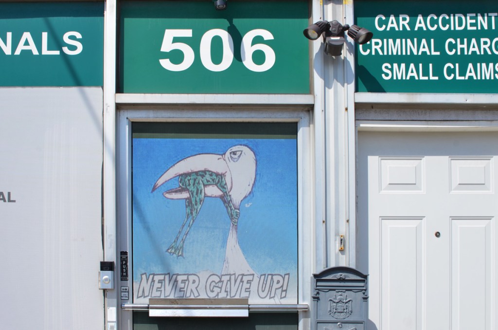 door with a window at 506 Oakwood, with a picture of a bird with a frog in its beak and the words Never give up 