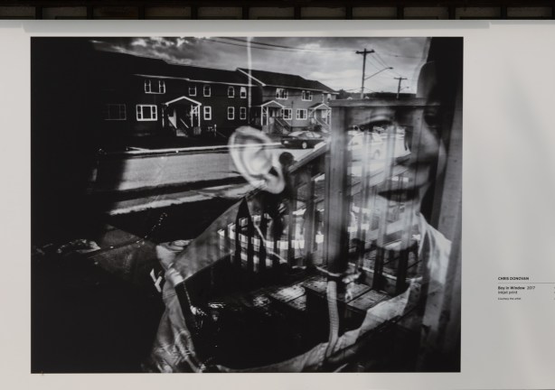 a black and white photo by Chris Donovan with reflections of a boy in a window and street scene below, on display outside Ryerson Image Centre 