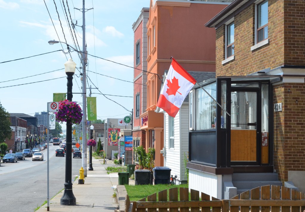a house with a glassed in front porch and a Canadian flag flying outside the door, other stores and houses in the background