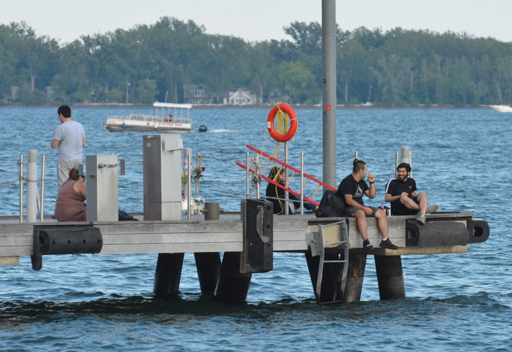 people sitting on the end of a dock by Lake Ontario