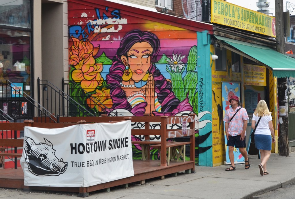 two people walking past a mural of a South American woman on Perolas Supermarket exterior wall