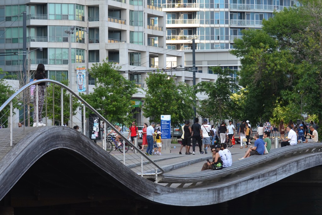 people sitting and walking on the Simcoe Wave Deck, Toronto waterfront, with condos behind