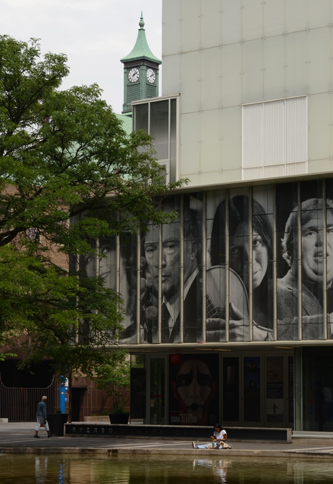 photographs of famous Canadians on the outer wall of Ryerson Image Center, with woman sitting on the concrete surrounding the reflecting pool by the entrance to R I C 
