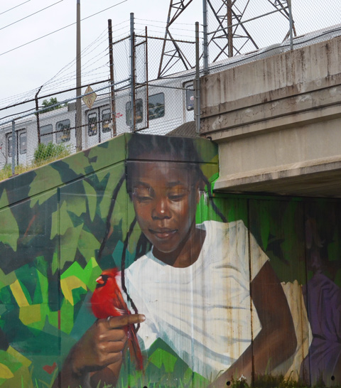 mural by Jarus of a young girl holding a cardinal bird, beside sidewalk on TTC subway underpass Pharmacy Ave in Scarborough, with a subway train passing by overhead