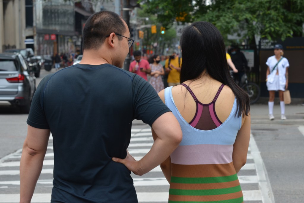 a couple, from the back, waiting to cross University ave., with a group of people waiting on the other side as well