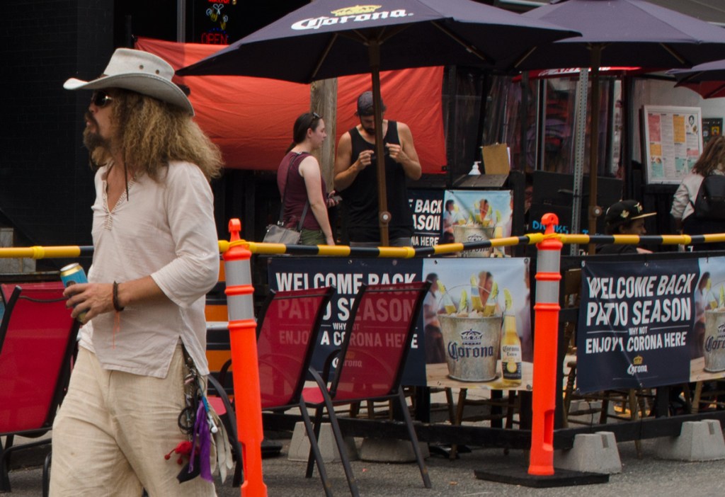 A man with long hair and wearing a cowboy hat walks past a patio in Kensington