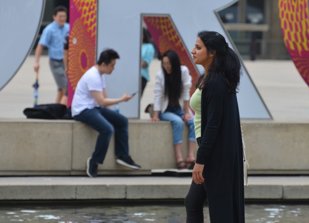 a young poses for a photo at Nathan Philips Square, people around the Toronto 3 d sign in the background