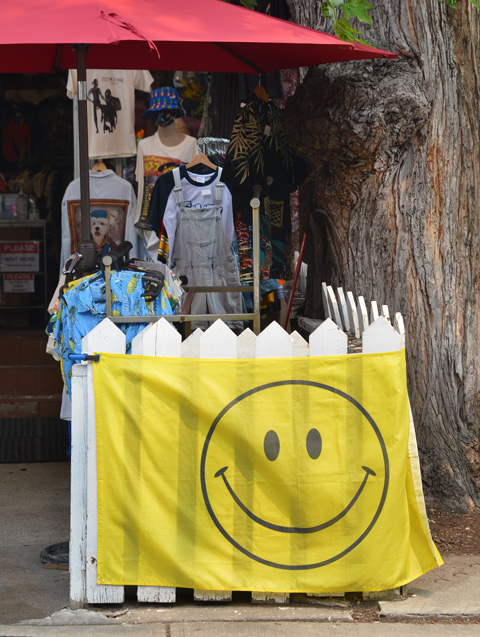 a large flag draped around a white picket fence, flag is yellow with a big happy face on it