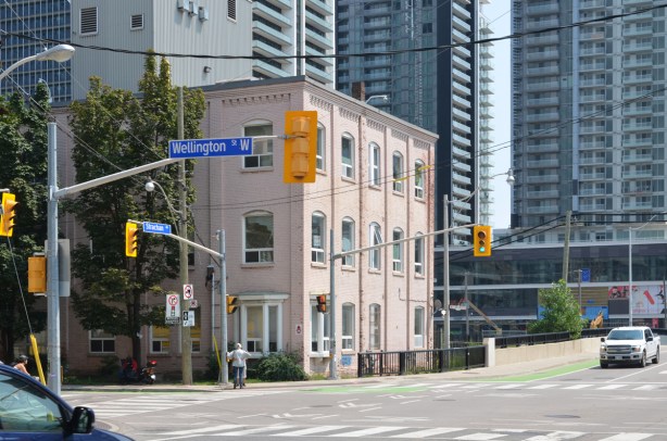 southeast corner of Bathurst and Wellington, pale pink three storey building on the corner, newer glass and steel condos behind