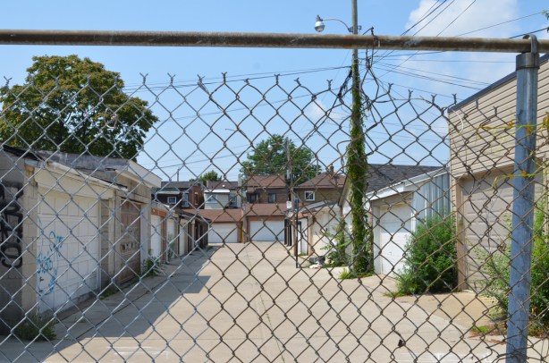an alley with garages on both sides, behind chainlink fence