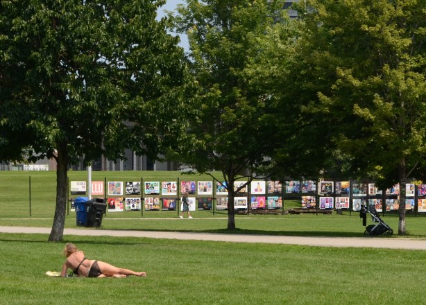 Garrison Common by Fort York, woman sun bather in bikini, art exhibit on fence surrounding the fort