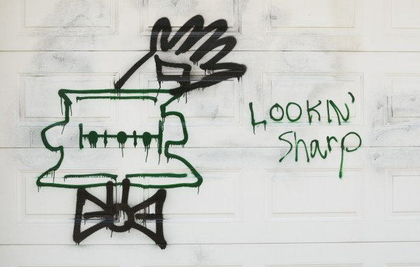 graffiti on a white garage door of a character's head with bowtie and one hand waving, words that say lookin' sharp 