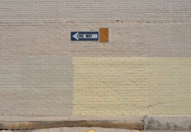 one way sign pointing left on beige brick wall 