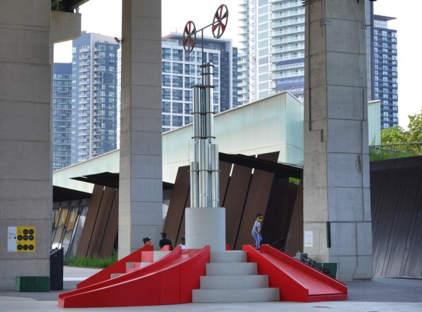 part of Playing in Public, an art installtion at the Bentway, small red slides with steps, in front of the old rusted metal walls near the entrance to Fort York