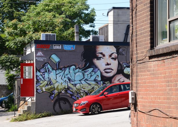 a red car is parked in front of a mural on the side of a building that has a red door at the back 