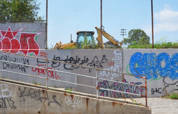 graffiti on concrete walls, with yellow digger parked behind fence