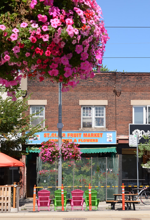 hanging basket of pink flowers across the street from St. Clair Fruit Market that has green and pink muskoka chairs outside