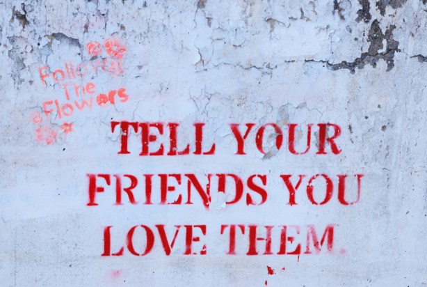 stencil on a concrete wall that says tell your friends you love them 